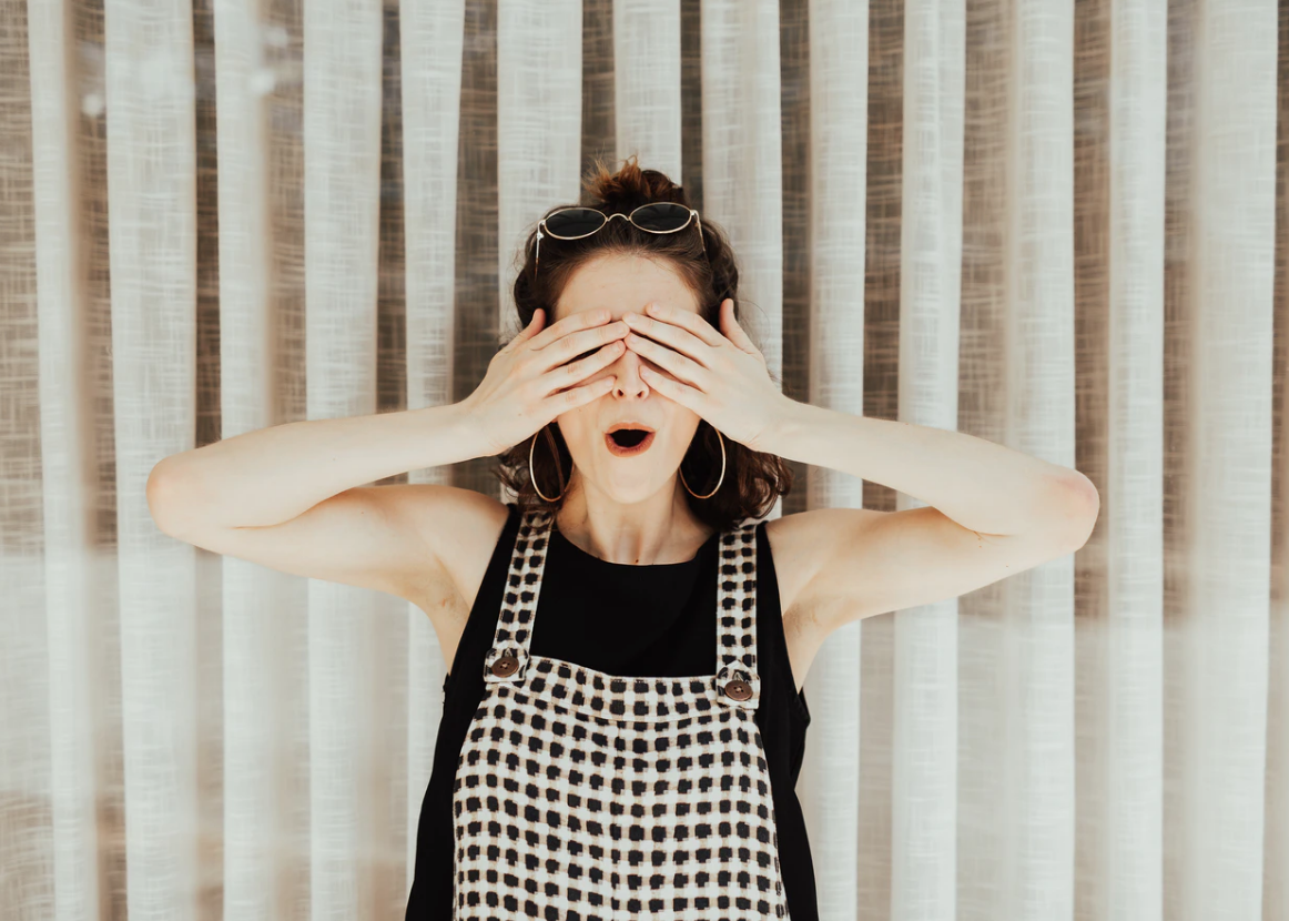 female wearing checkered overalls covers her eyes, picking a university