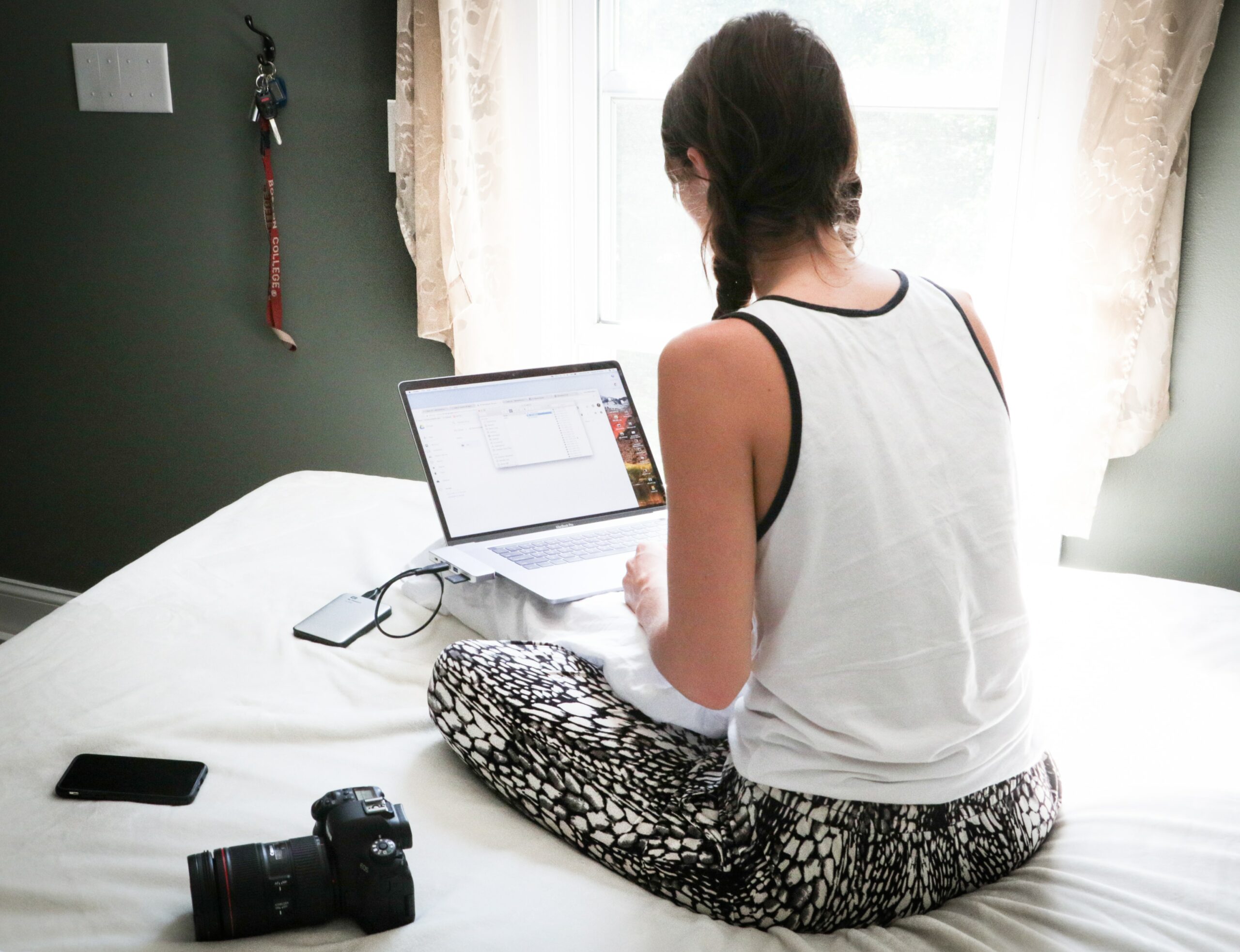 Girl sitting cross-legged on a bed with a laptop on her lap